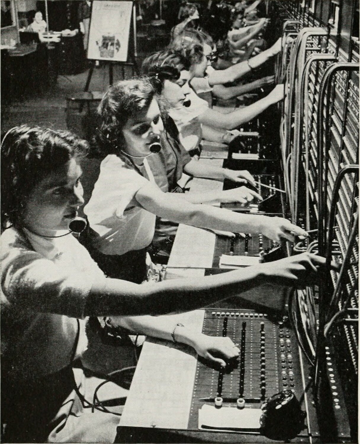 Rows of switchboard operators routing calls across a wall of sockets and cords.